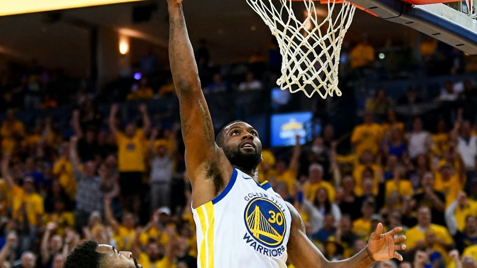 NBA球员高高跃起单手扣篮，篮球即将入筐，对手防守球员仰头观望，现场观众起立欢呼